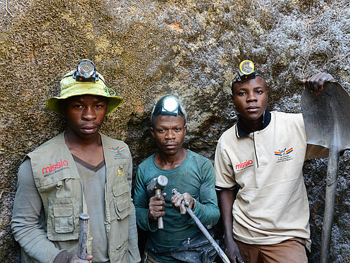 Drei Minenarbeiter stehen mit ihren Arbeitsgeräten in einer Mine im Kongo.